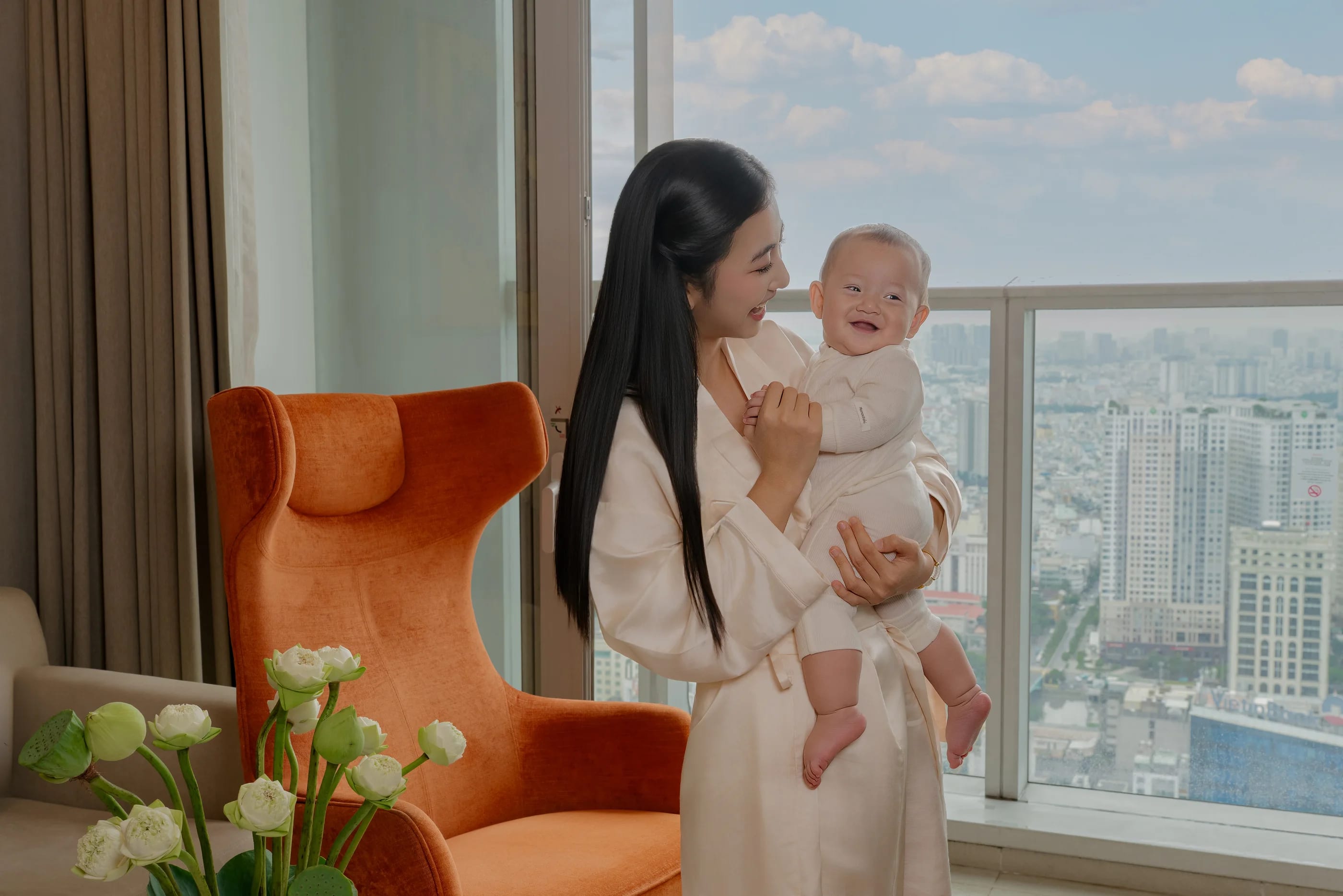 A mother holding her smiling baby by the suite's glass wall above Saigon