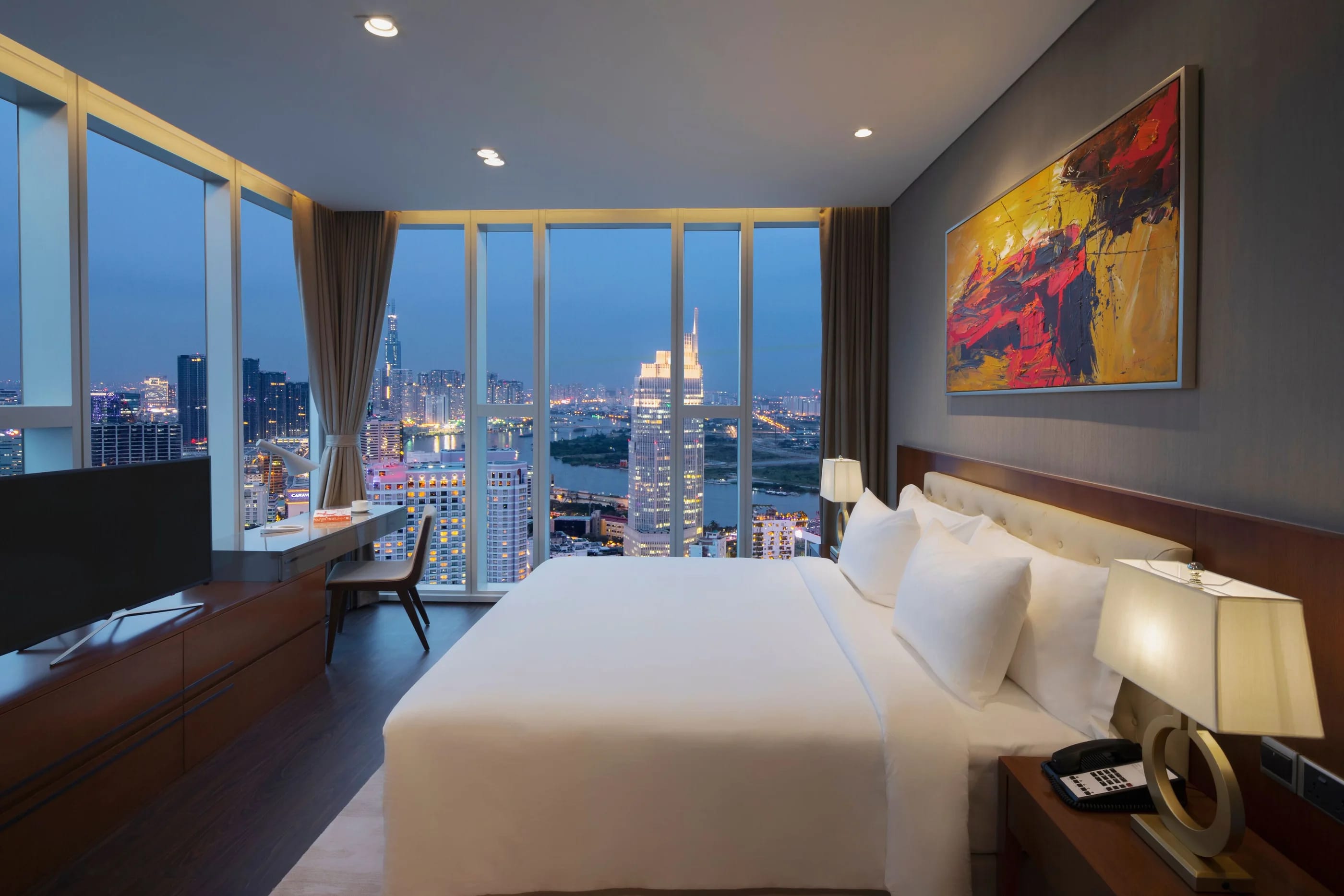 A Casa suite at dusk, floor-to-ceiling windows looking out over the Saigon River and the city lights