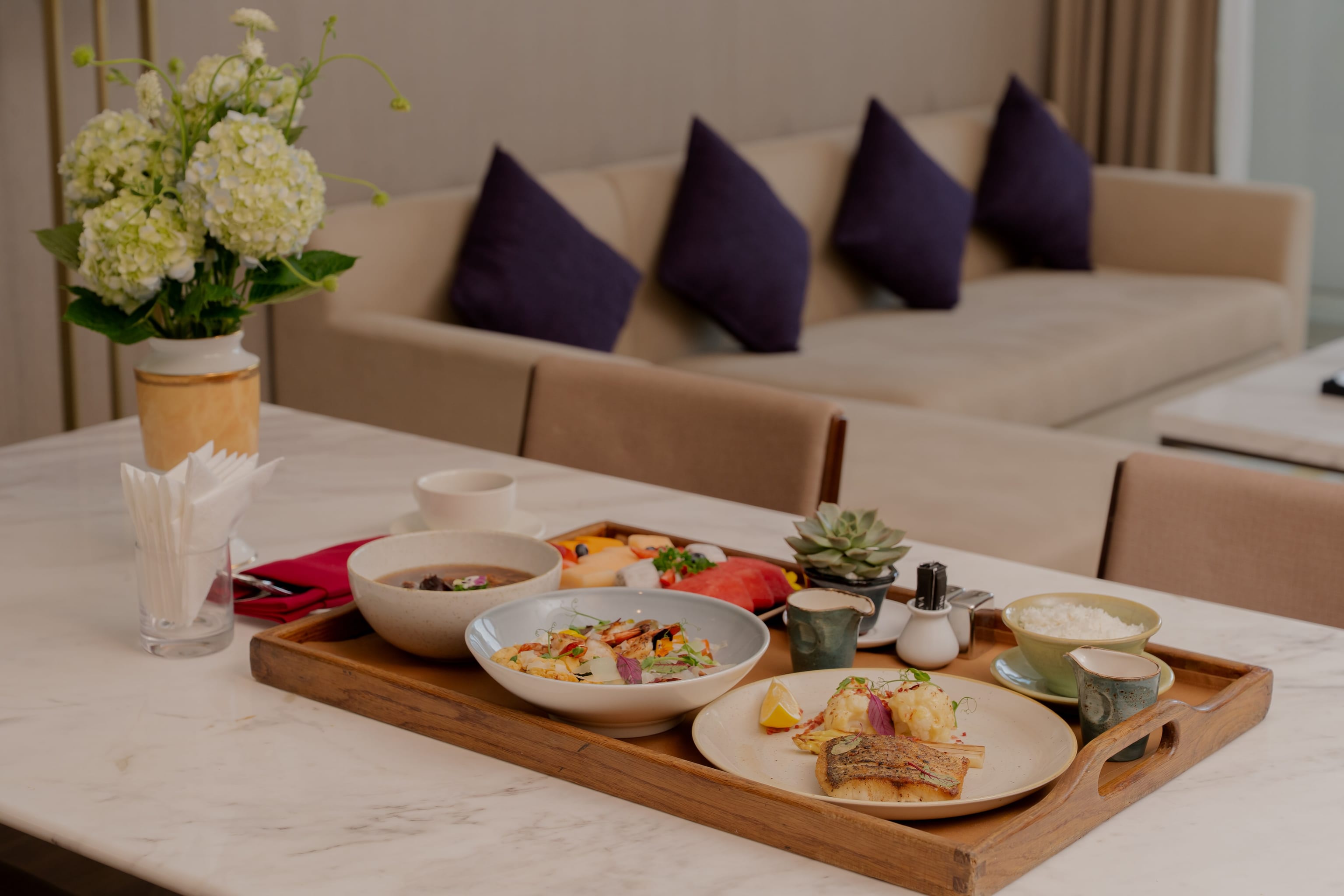 An open recovery meal with fish, broth, multigrain rice, greens, fruit and warm tea on a walnut tray