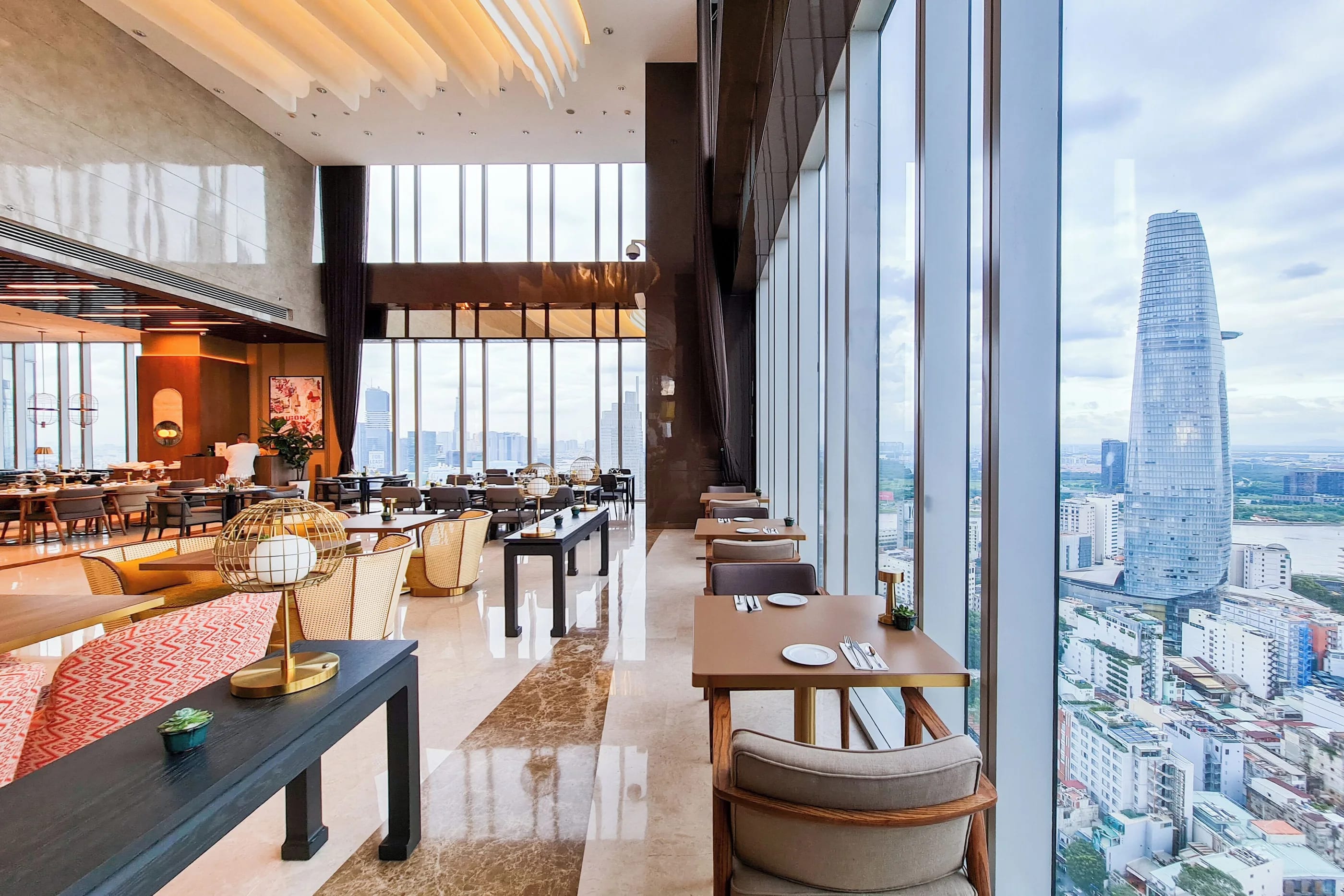 A high-floor dining room with tables along a glass wall looking out over the city